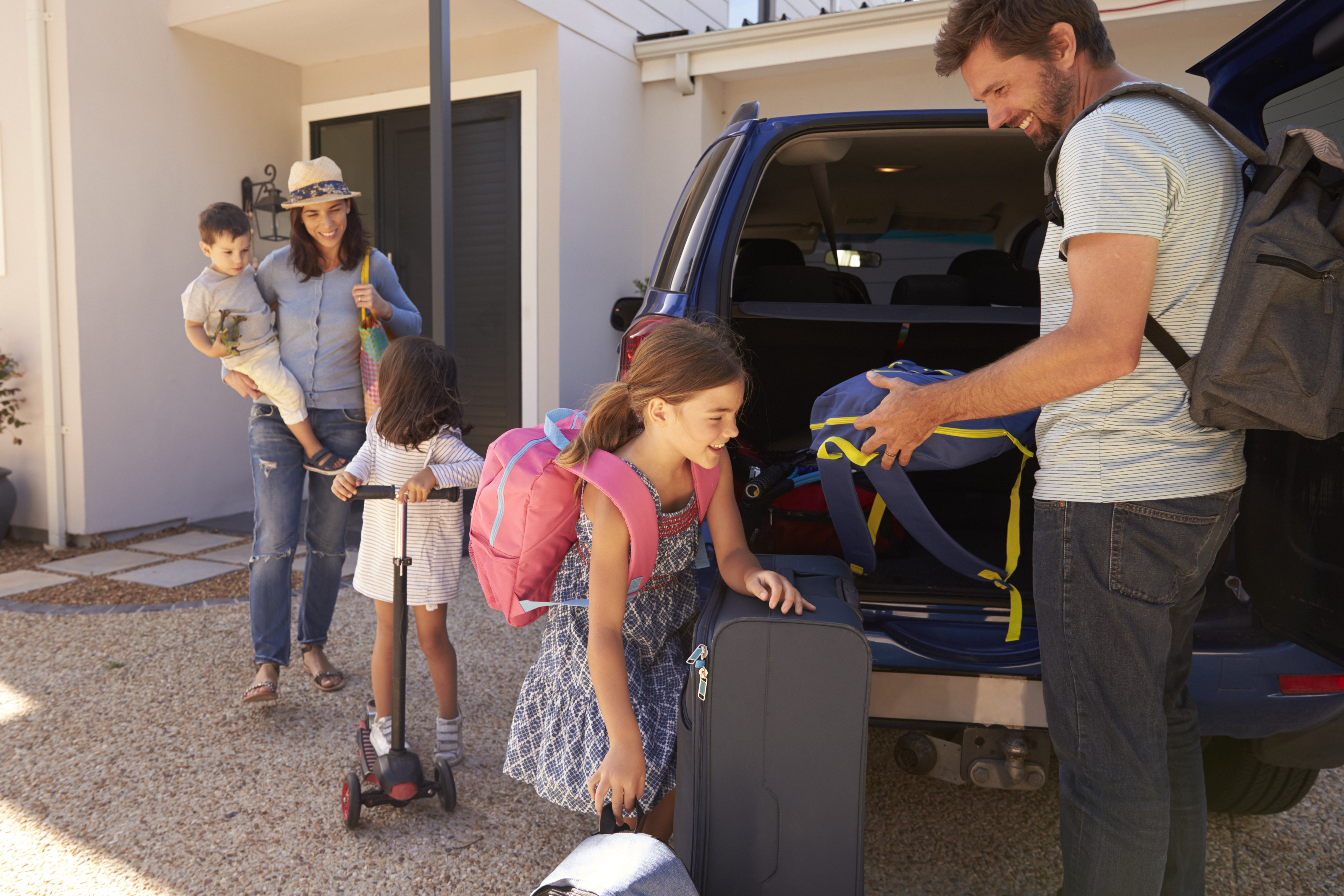 Young family packing suitcases and belongings into a vehicle.