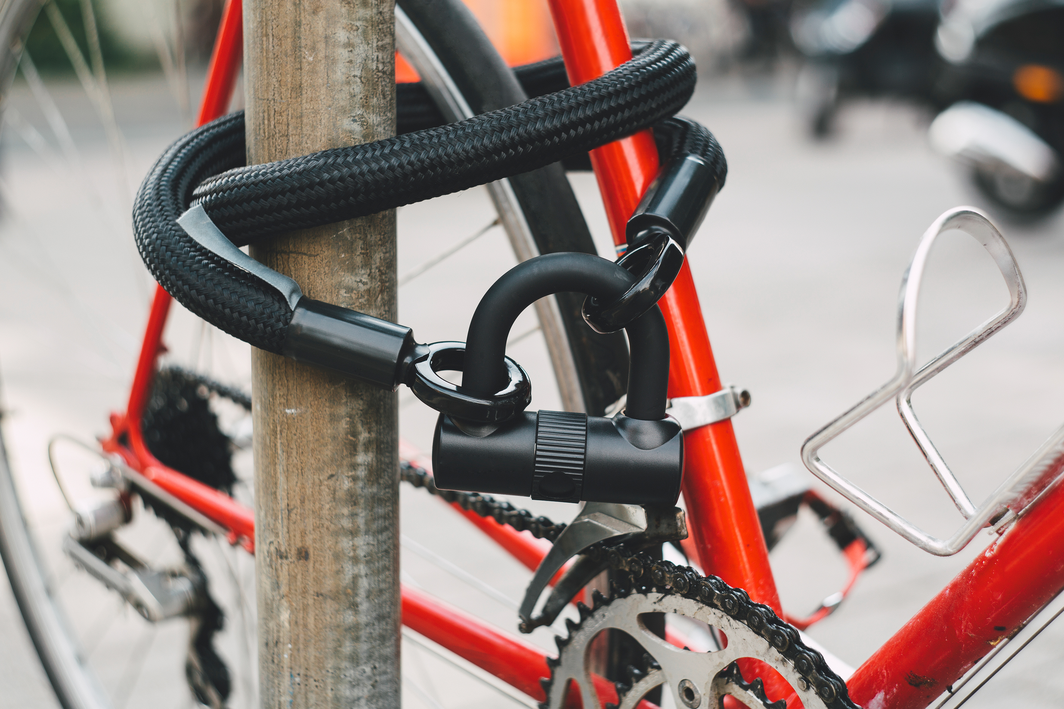 Red bicycle locked to pole with heavy-duty black bike lock.