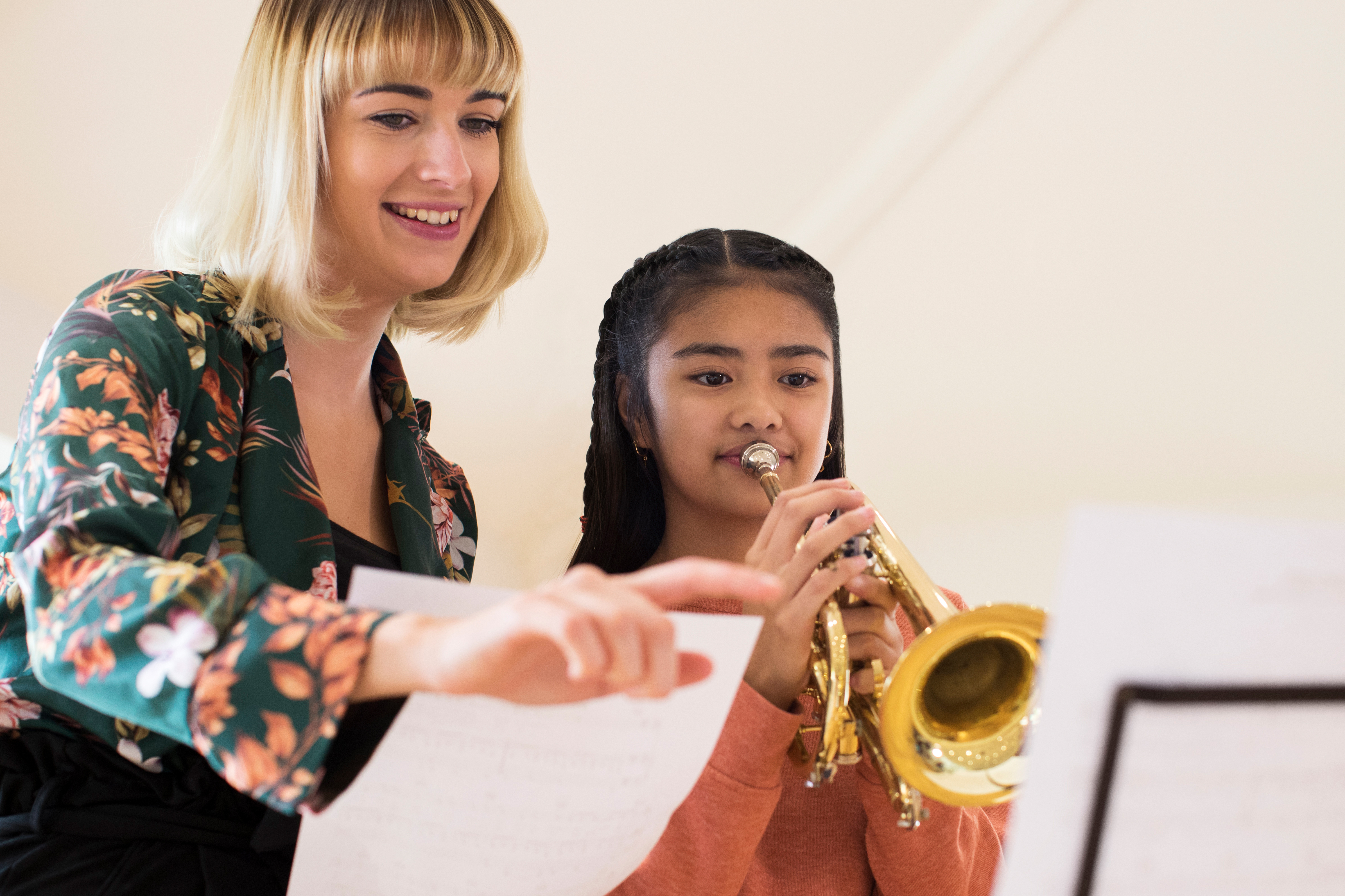 Young woman teaching a girl to play trumpet, looking at music.