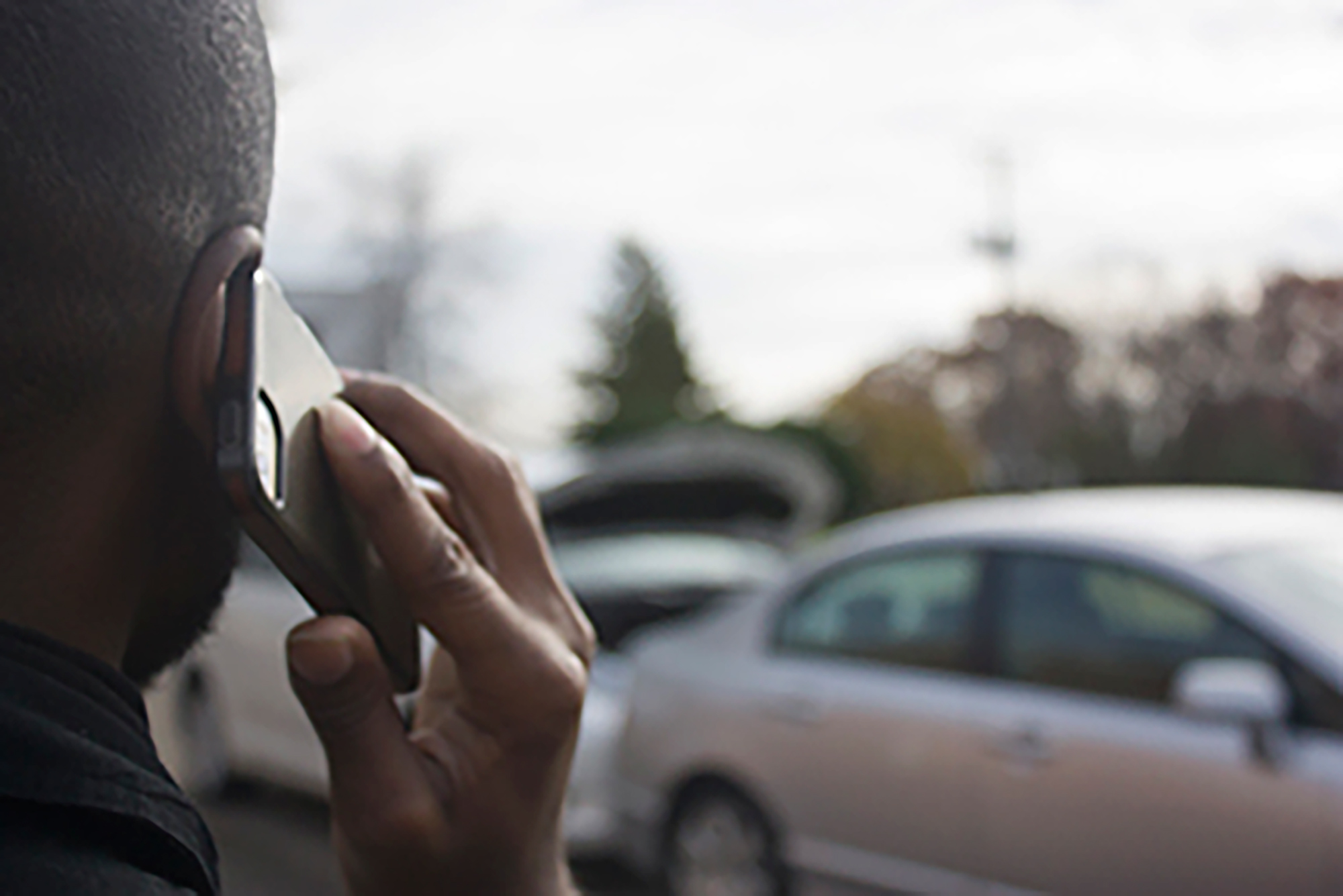 Person on the phone with two cars in background.