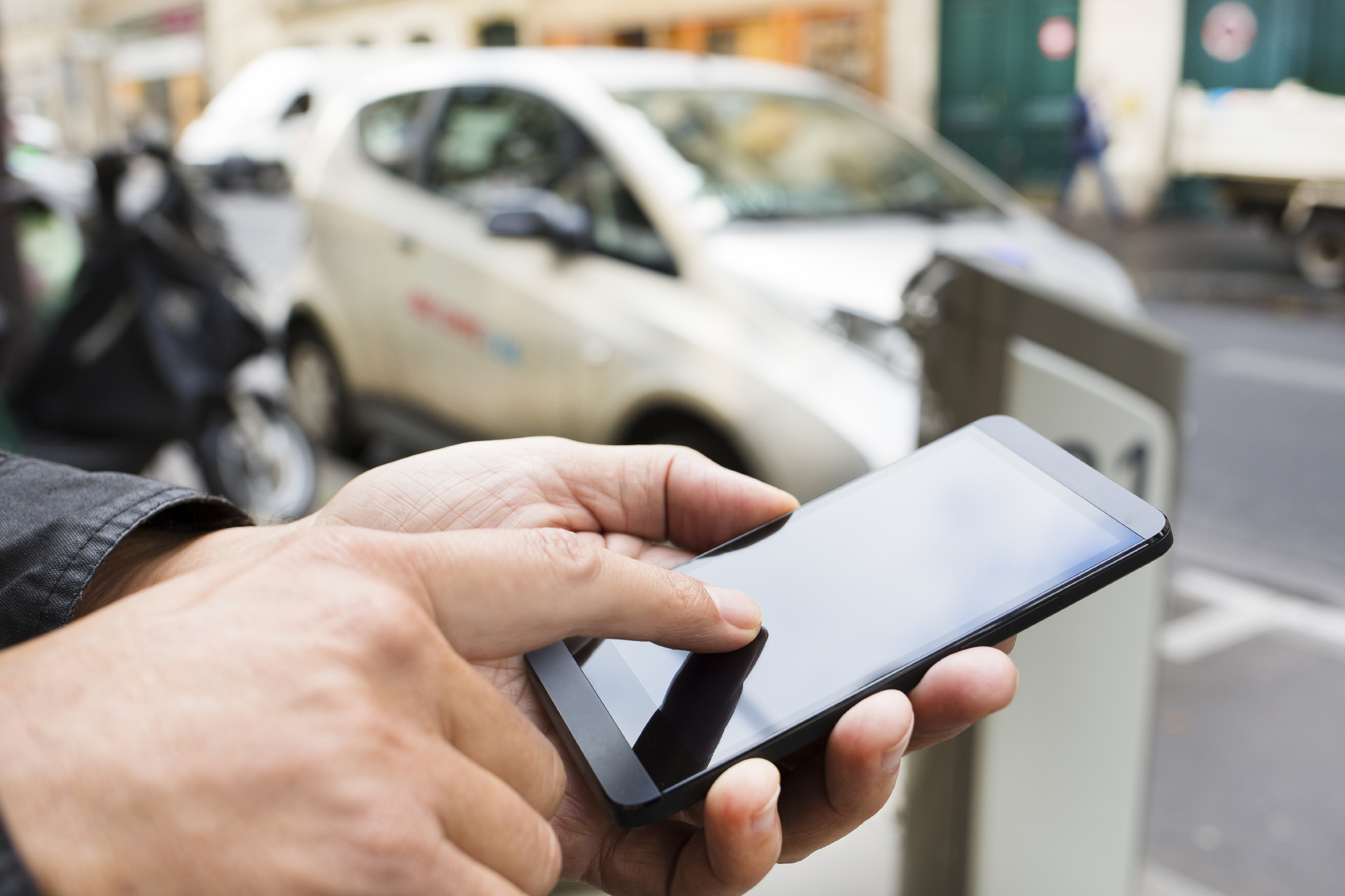 Close-up of a person holding a cellphone with out-of-focus car in the background.