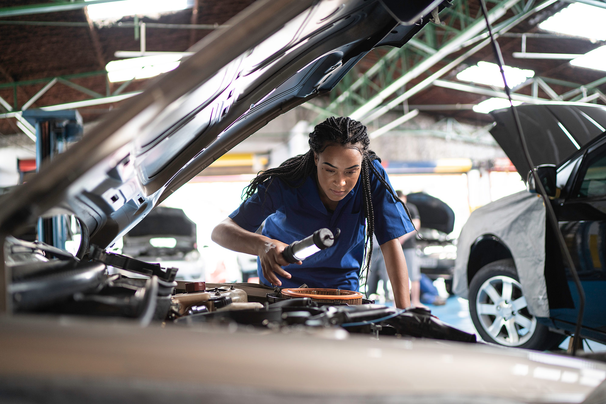 A female mechanic bent over while examining vehicle engine.