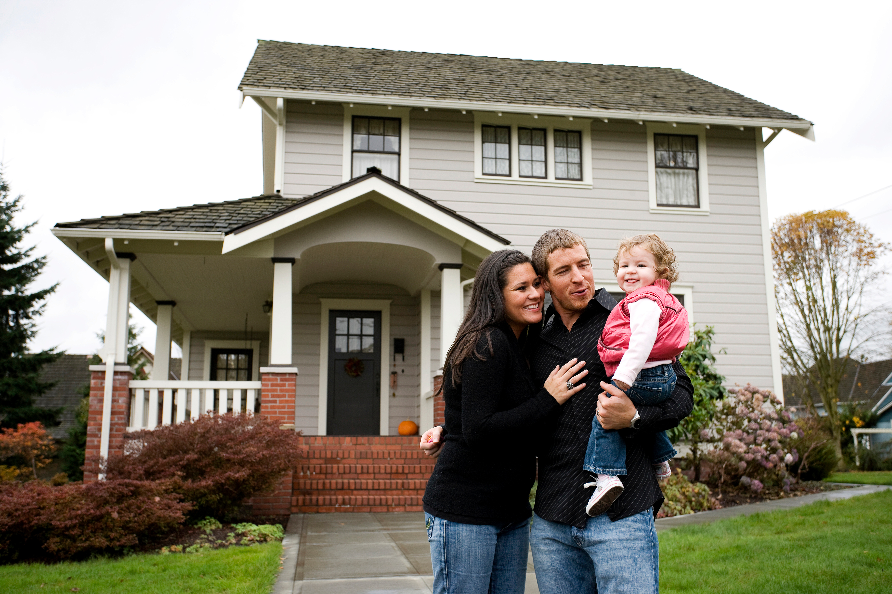 Family of three standing in front of two-story home.