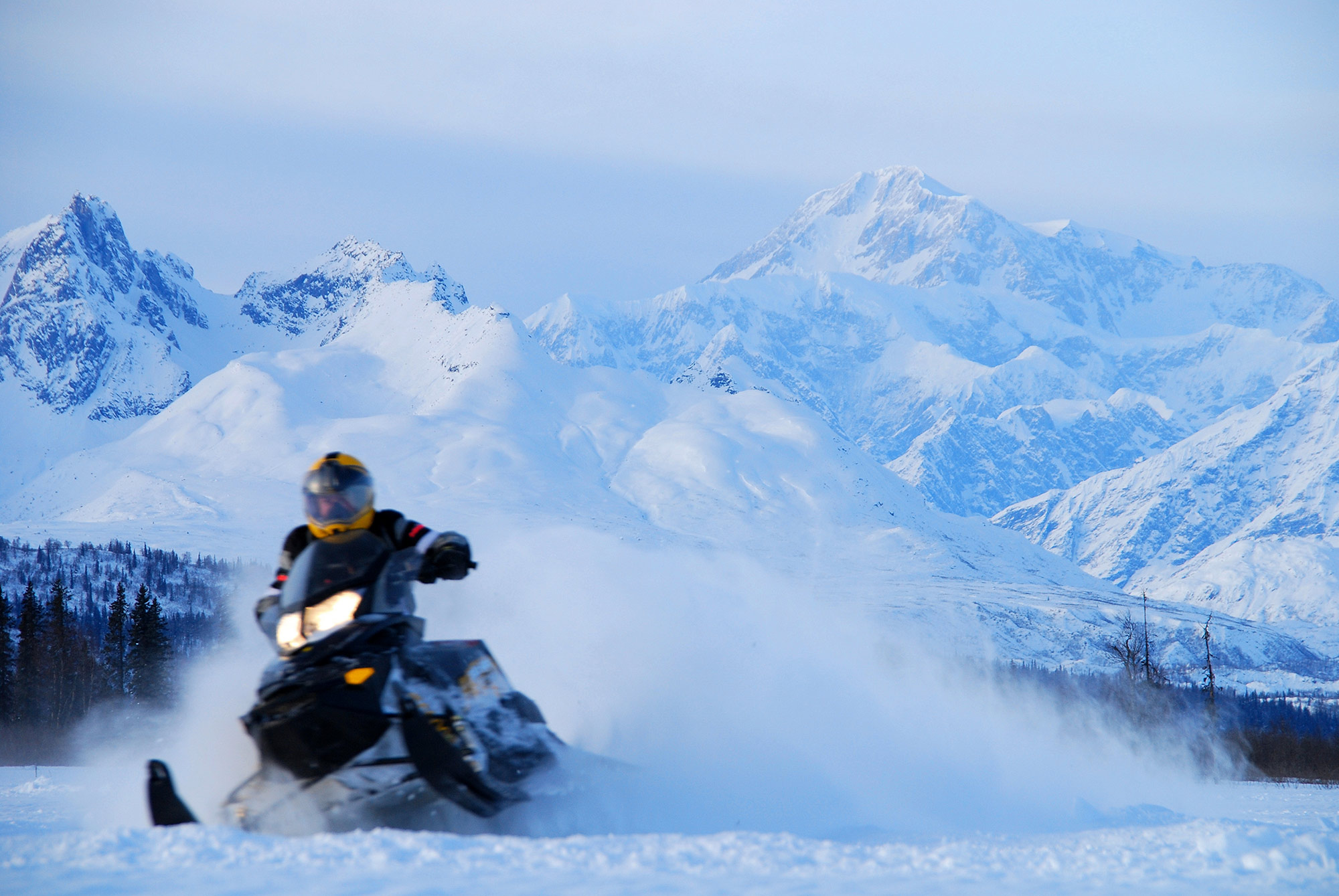 A person riding a snowmachine through the snow in a mountainous area.